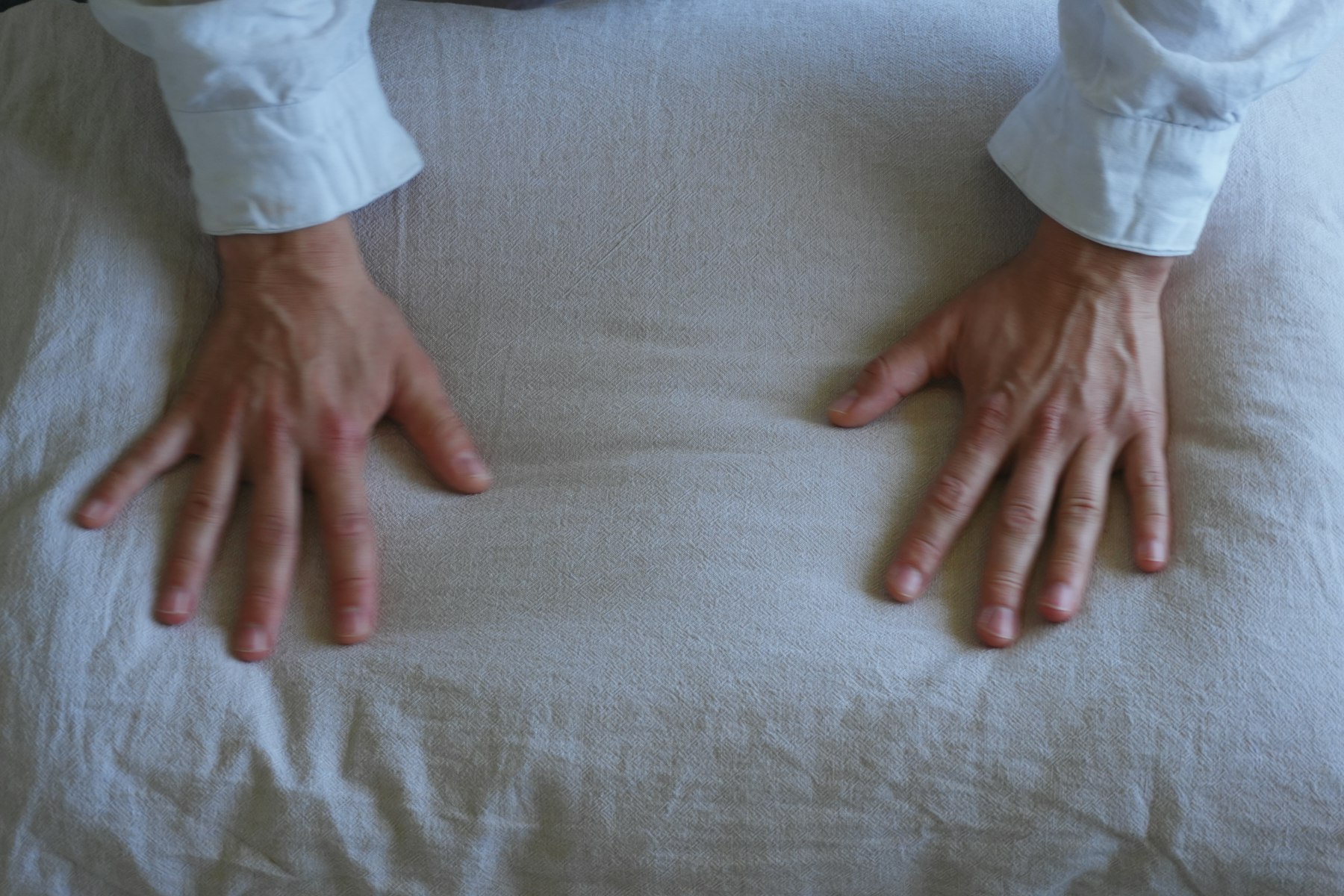 Two hands resting flat on soft linen, fingertips and nails relaxed